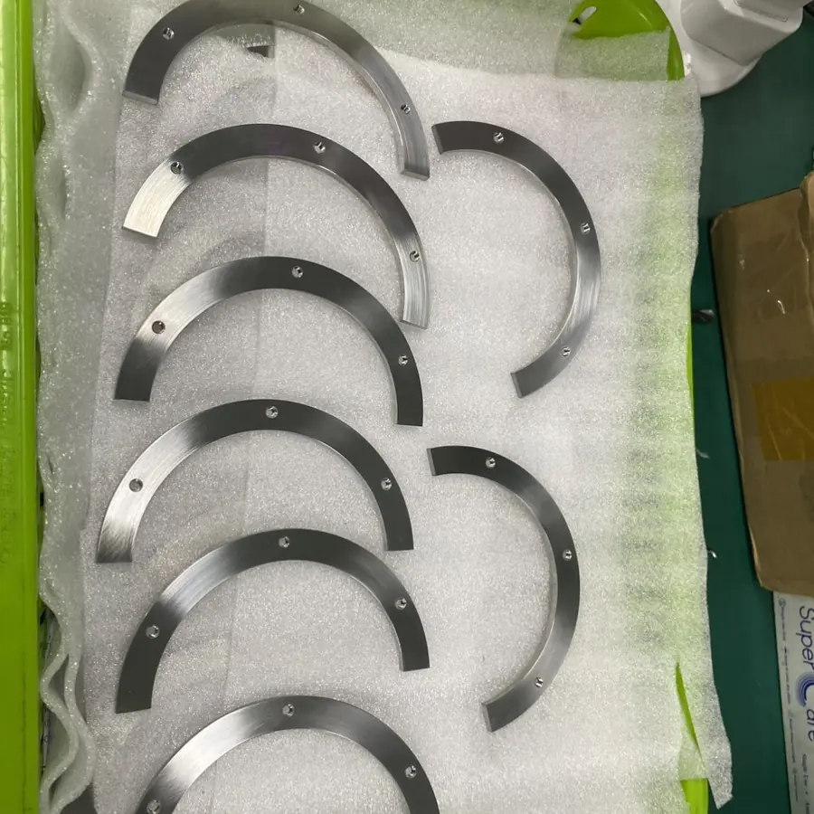 Set of CNC machined arc segments with small drilled holes along the edge, packed on foam
