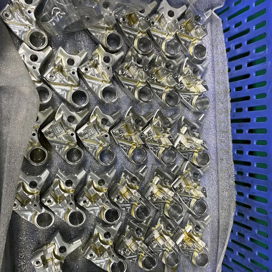 Batch of CNC milled brackets with pockets, bores and gold-colour finish, bagged in a crate