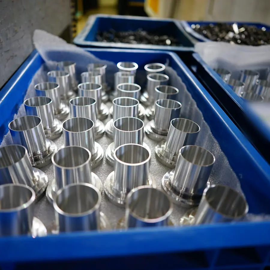 Batch of CNC turned flanged sleeves standing on foam in blue inspection trays