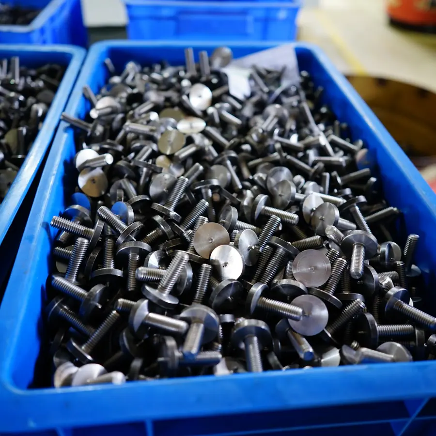Crates of CNC turned flat-head screws with wide thin heads and threaded shanks