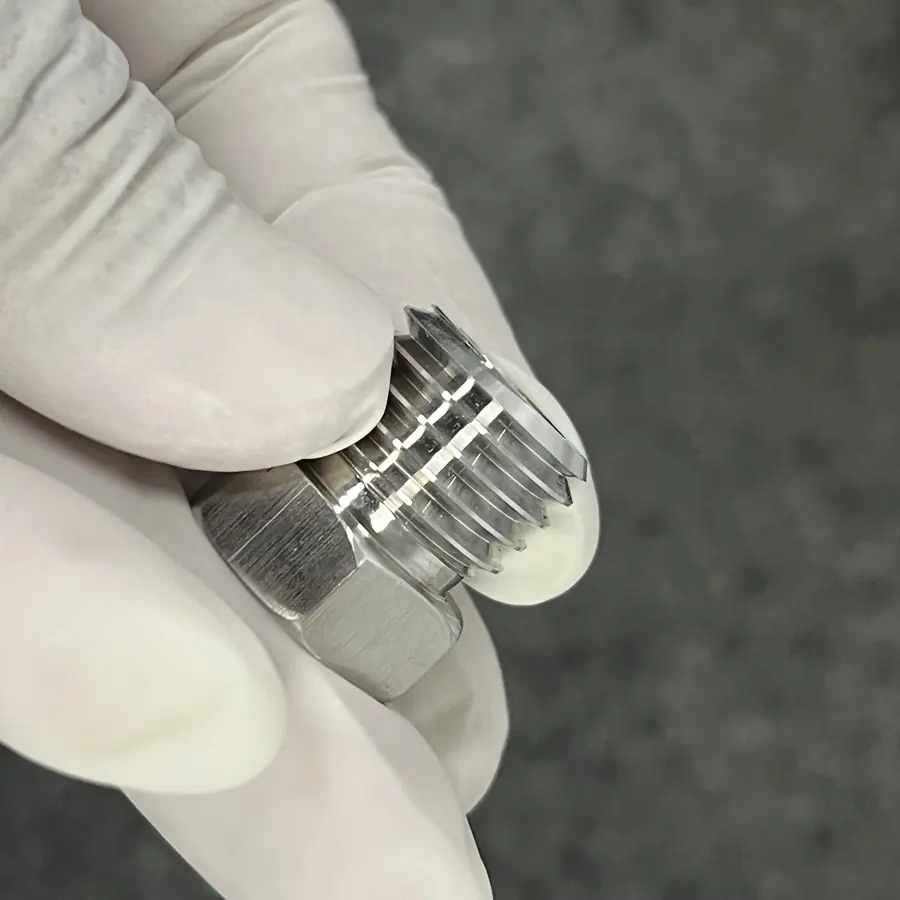 Close-up of a CNC turned hex threaded plug with clean thread crests, held in a gloved hand
