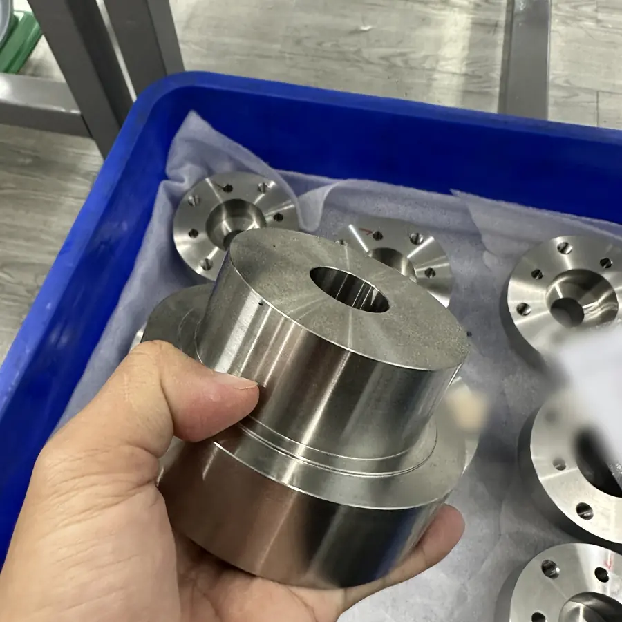 CNC turned stepped flange hub with centre bore, bolt-circle flanges in the tray behind