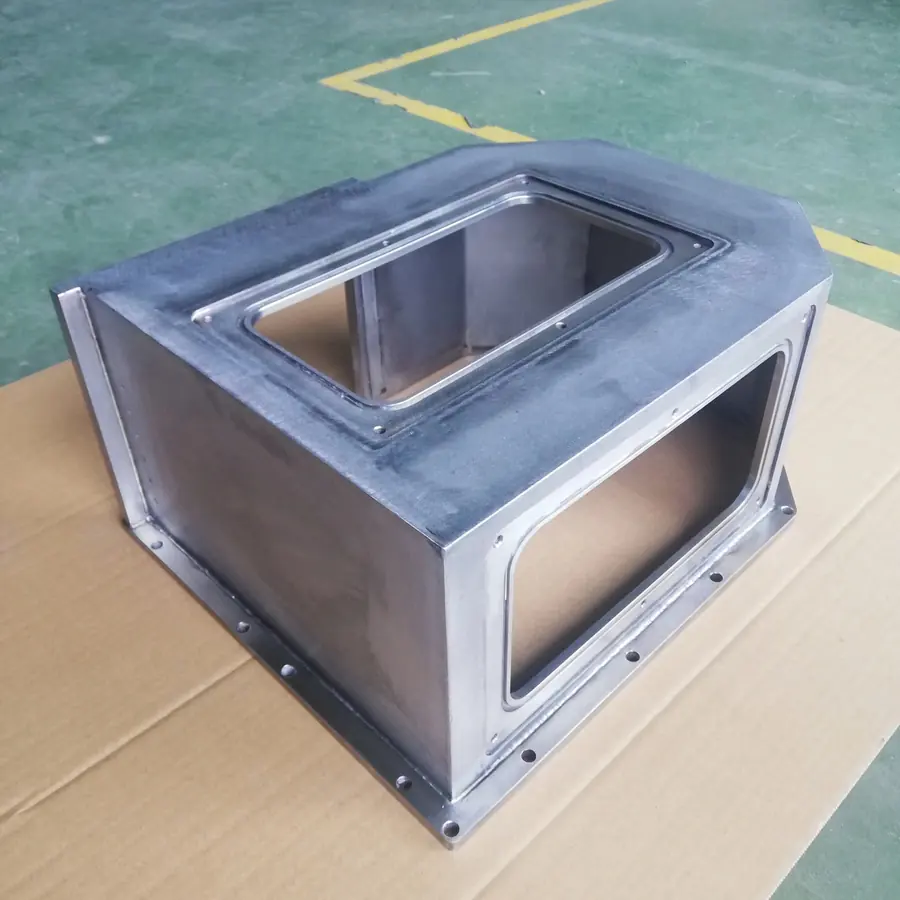 Welded plate housing with machined window frames and a drilled mounting flange